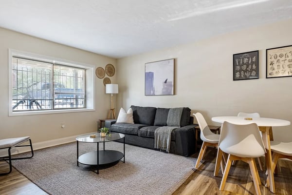 Open-plan living room with black sofa, round coffee table, dining area, and water view from large windows
