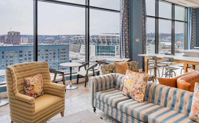 High-rise lounge with striped seating, floor-to-ceiling windows overlooking waterfront stadium and city skyline